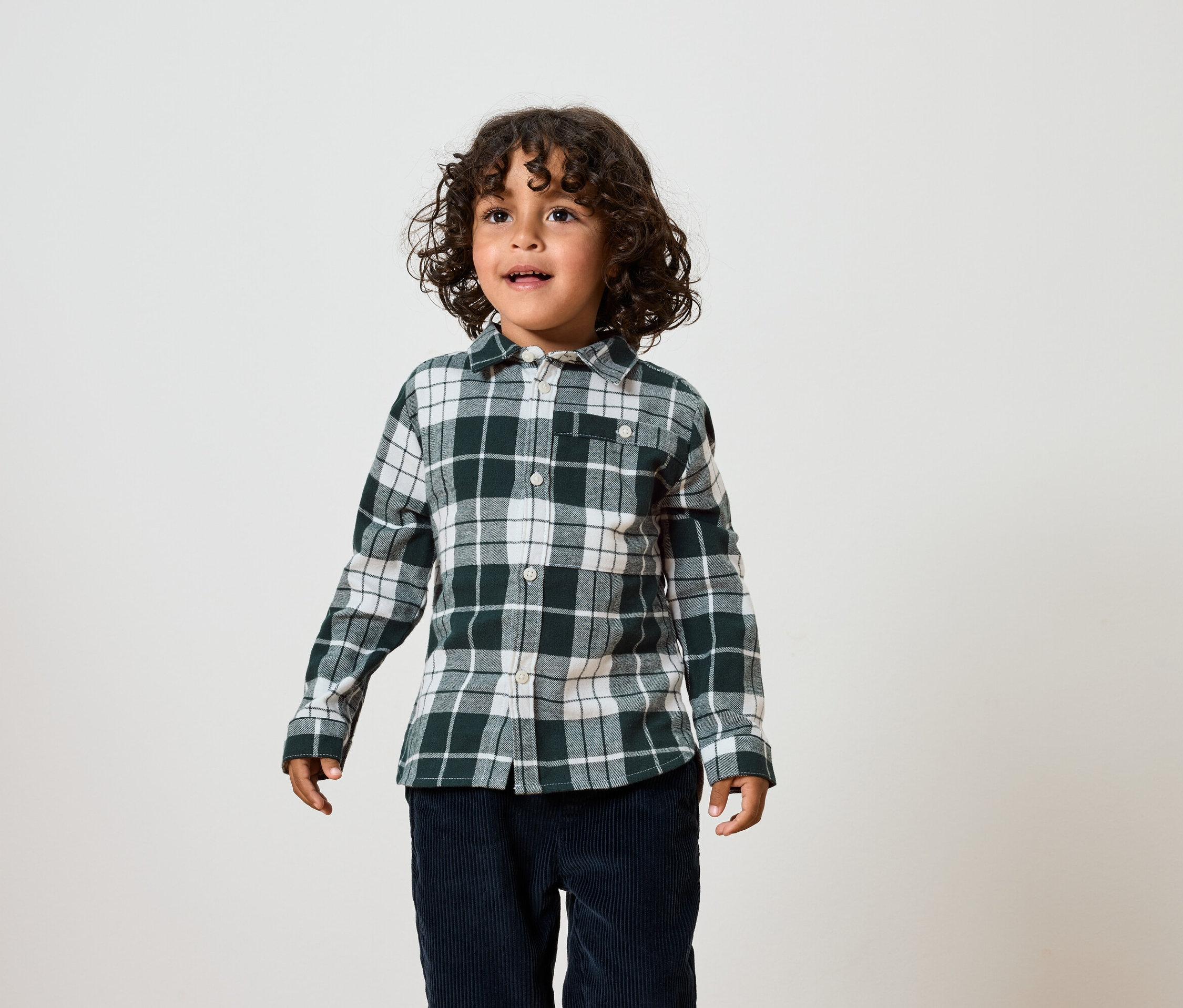 Egy göndör hajú fiú zöld-fehér kockás inget és sötétkék nadrágot visel.