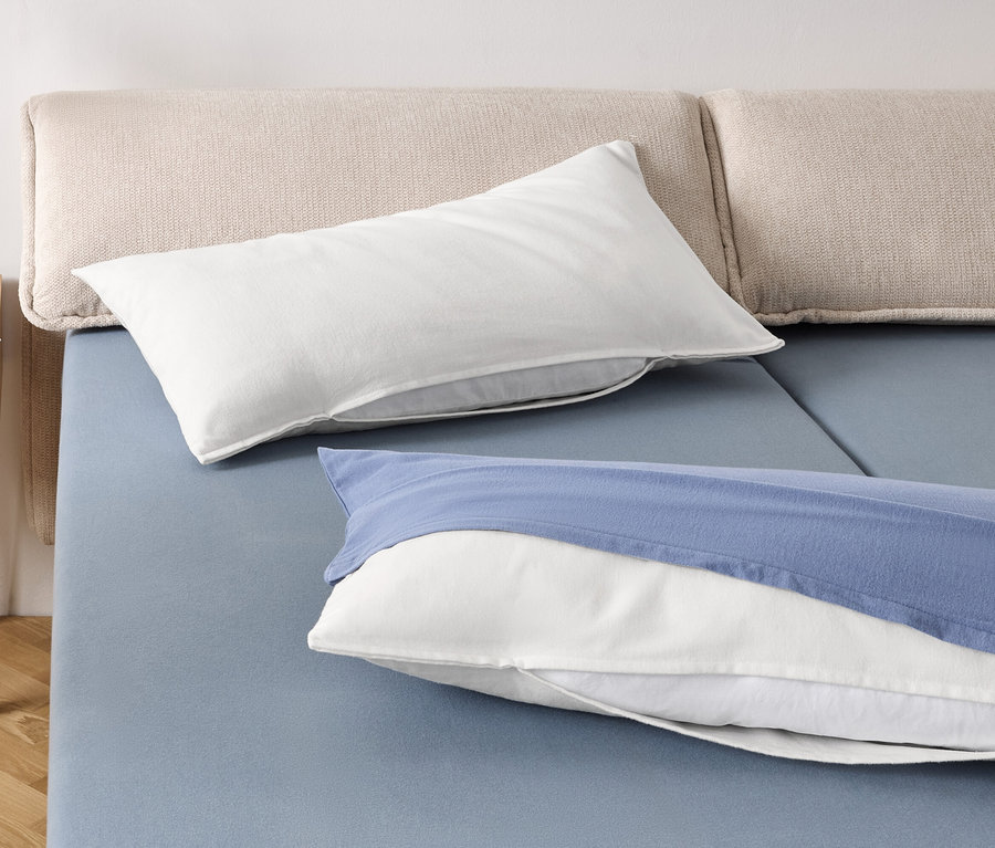 Két fehér párna és egy kék huzatú fehér párna egy kék ágyon.