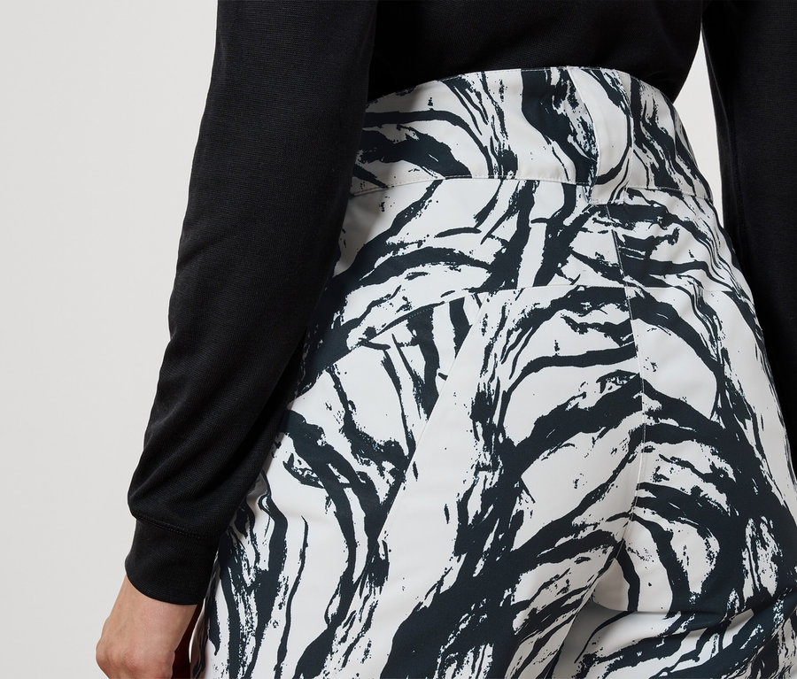 Hátulnézet egy fekete felsőt és fekete ágmintás fehér nadrágot viselő nőről.