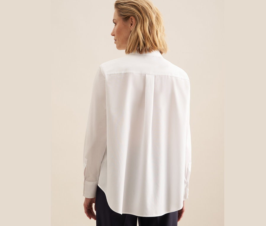 Hátulról látható egy nő fehér, vasalásmentes Seidensticker blúzban.
