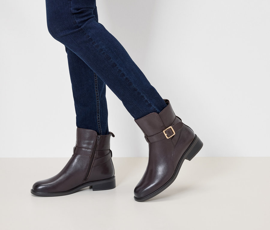 Sötétkék farmerben és barna bőr bokacsizmában lábak, csattal és arany csattal.