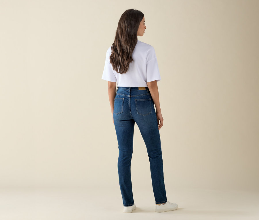 Egy nő háttal áll a kamerának, és egy Slim-Jeans – Fit »Emma«, középkék farmernadrágot, egy fehér pólót és tornacipőt visel.