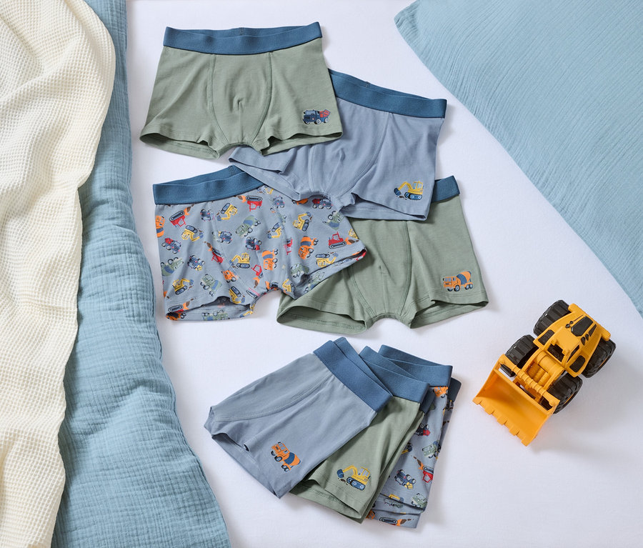 Egy ágyon több fiú boxeralsó autó mintával és egy sárga játék buldózer.