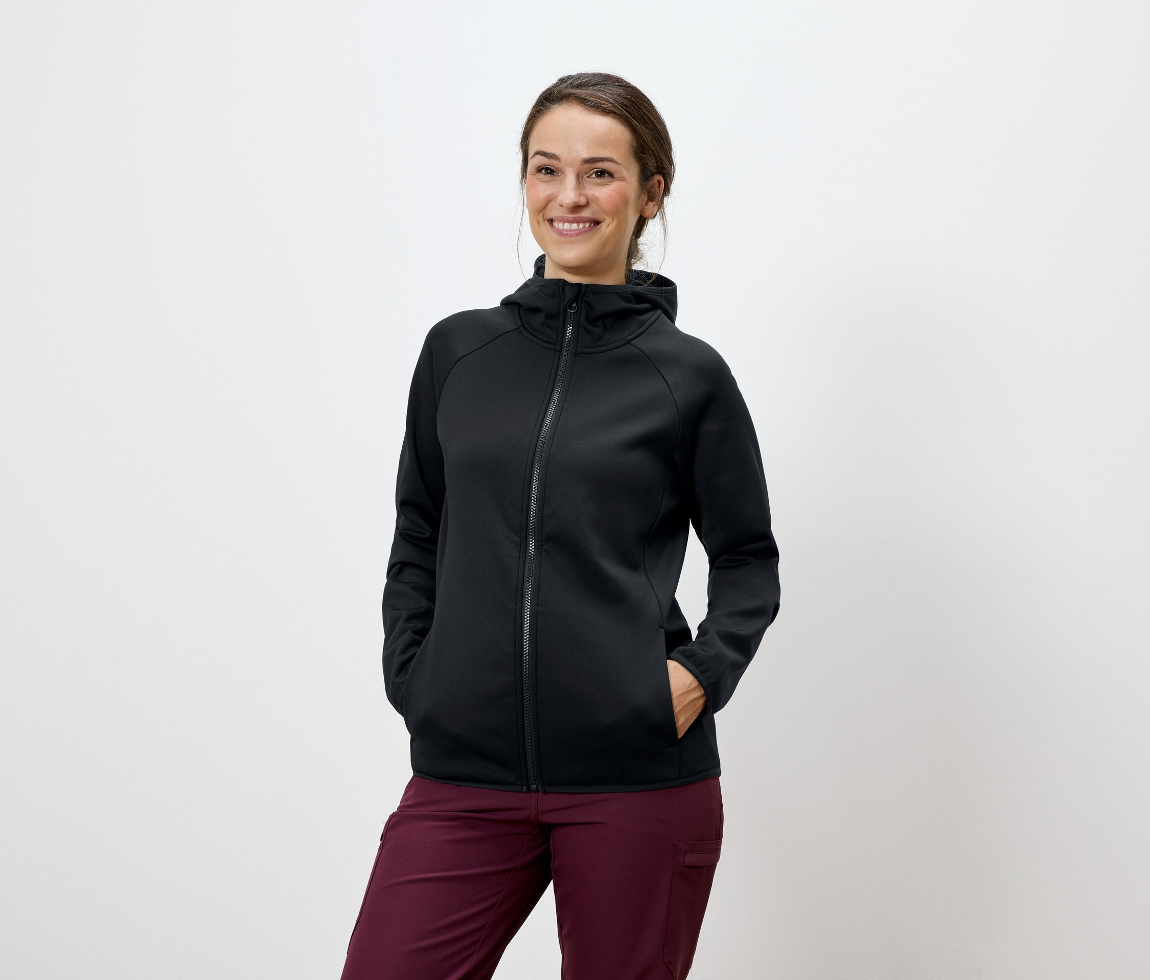 Nő pózol fekete kapucnis pulóverben és bordó nadrágban.