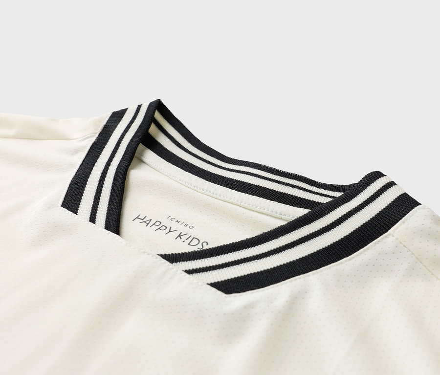 Egy fehér póló részletfotója fekete-fehér csíkos gallérral és 'TCHIBO HAPPY KIDS' logóval.