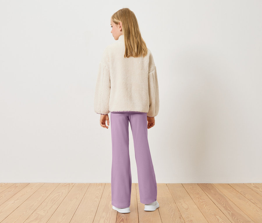 Hátulnézet egy szőke lányról, aki krémszínű teddy fleece felsőt és lila nadrágot visel.