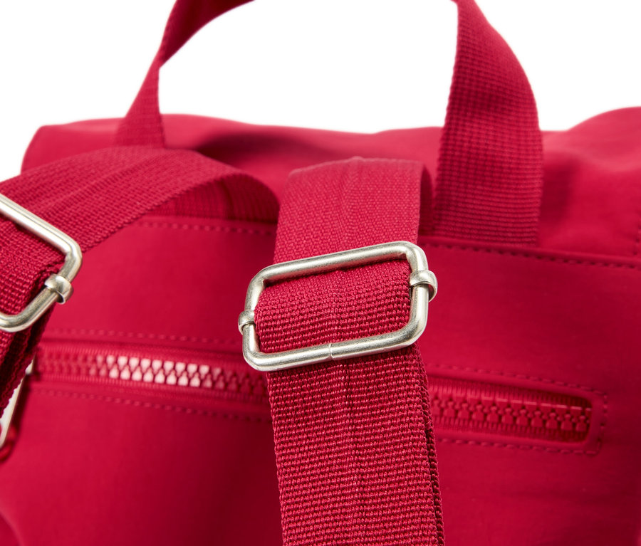 Egy piros hátizsák közeli képe ezüst csatokkal a pántokon.