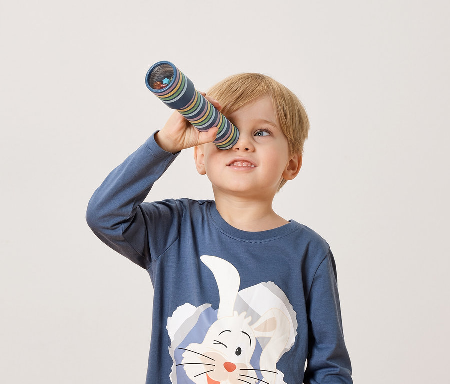 Egy szőke fiú egy kaleidoszkópon keresztül néz.