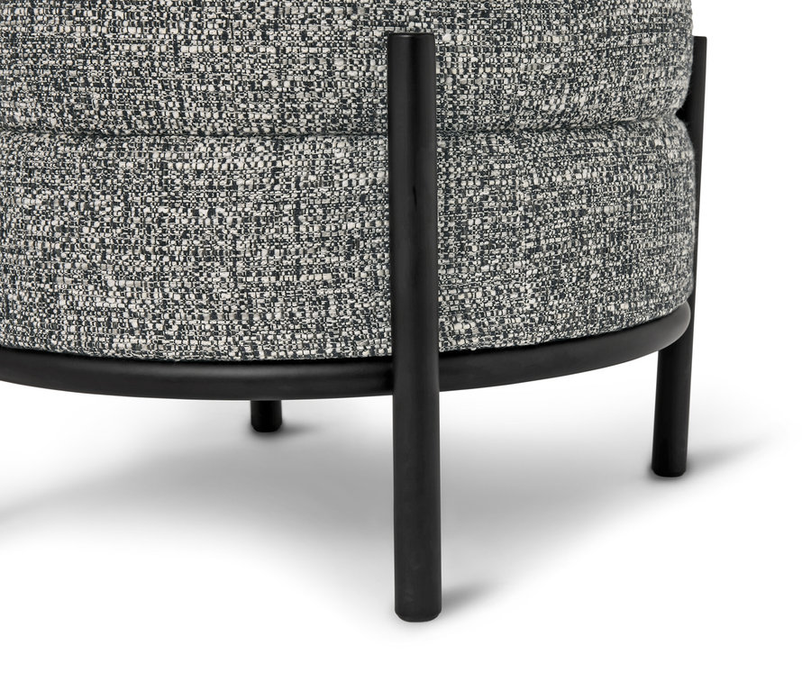 Egy szürke mintás szövetkárpitozású és fekete fém lábú, kerek ülőke közeli képe.