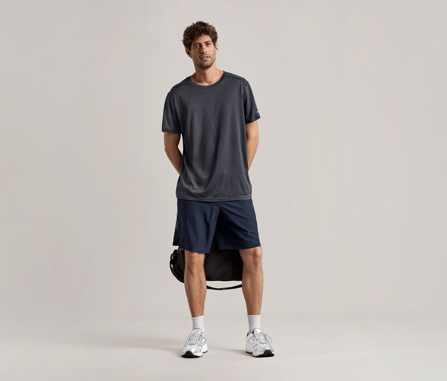 Egy férfi áll világos háttér előtt, antracit színű sportfelsőben, rövidnadrágban és sportcipőben.