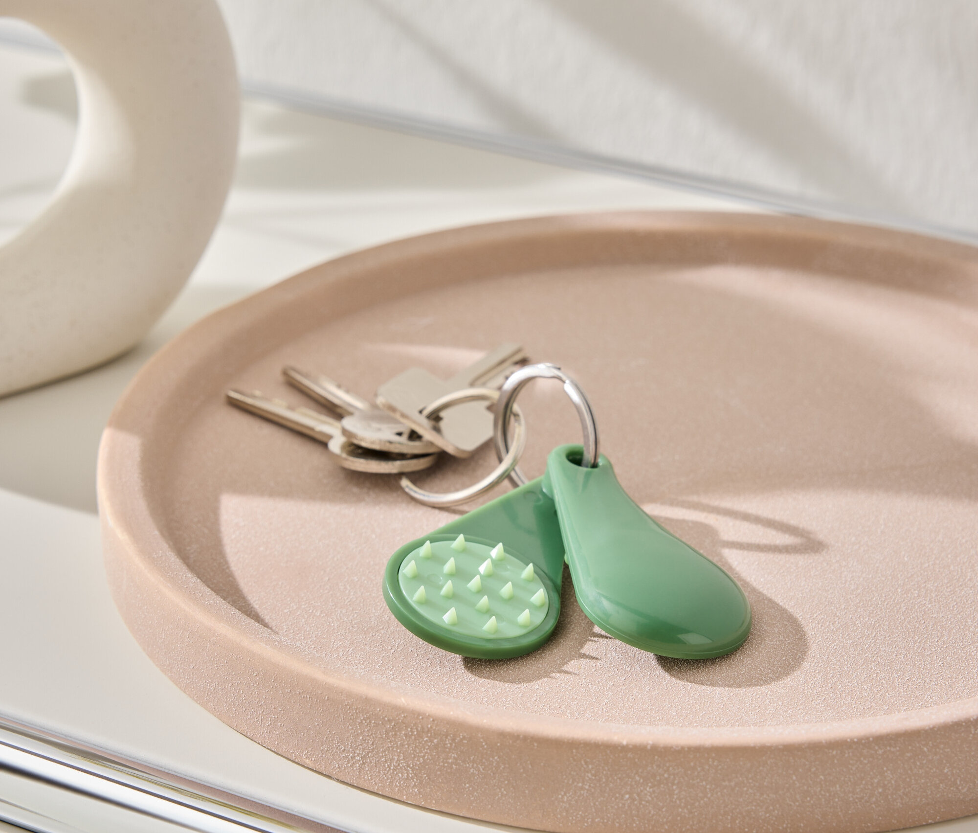 Kulcsok és zöld kulcstartó fekszik egy rózsaszín tányéron.