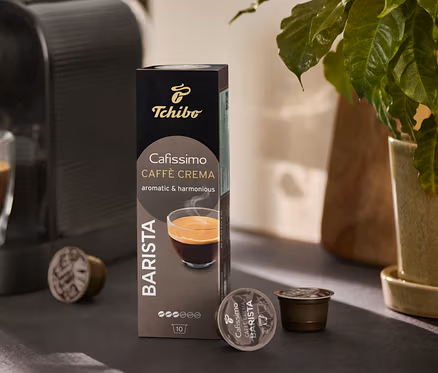 Kávéfőző tölt egy poharat kávéval. Mellette egy csomag Cafissimo BARISTA Caffè Crema és néhány kapszula látható.