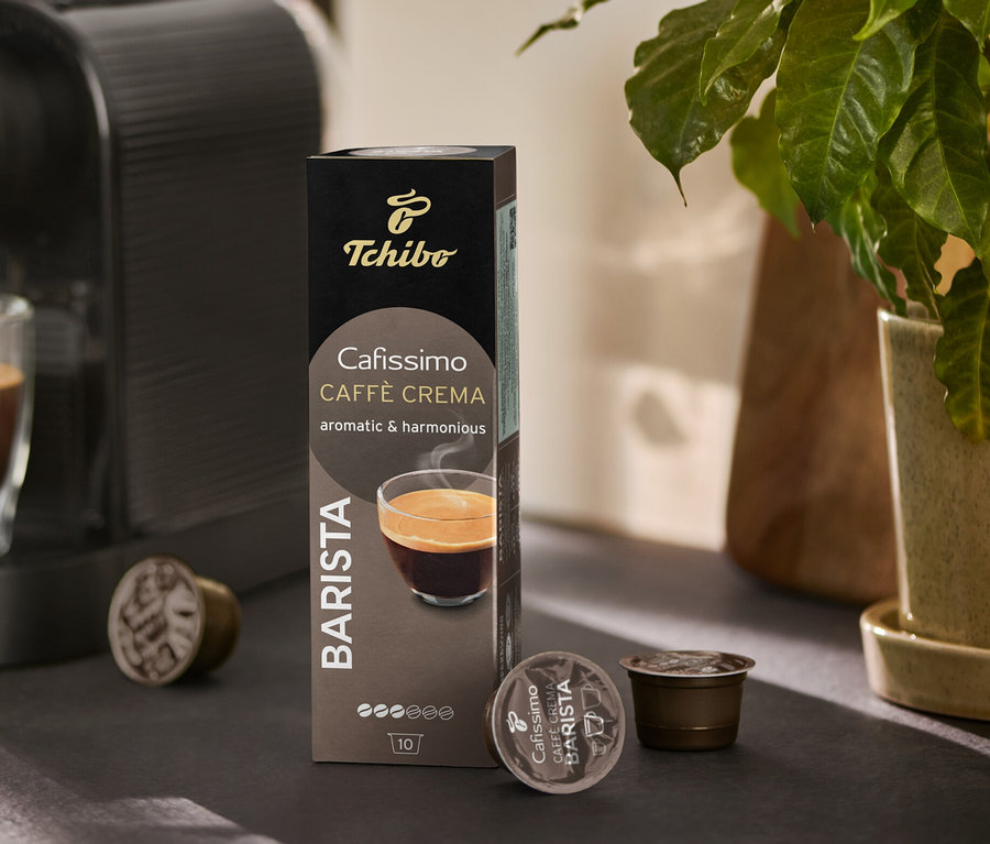 Kávéfőző tölt egy poharat kávéval. Mellette egy csomag Cafissimo BARISTA Caffè Crema és néhány kapszula látható.