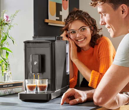 Két ember nézi, ahogy a kávé folyik a »Esperto2 Caffè« automata kávéfőzőből két pohárba.