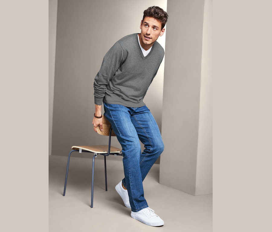 Egy férfi ül egy széken és V-nyakú pulóvert visel.