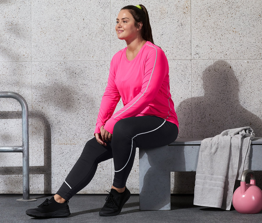 Nő ül egy padon, neonpink színű funkcionális felsőben és sportnadrágban.