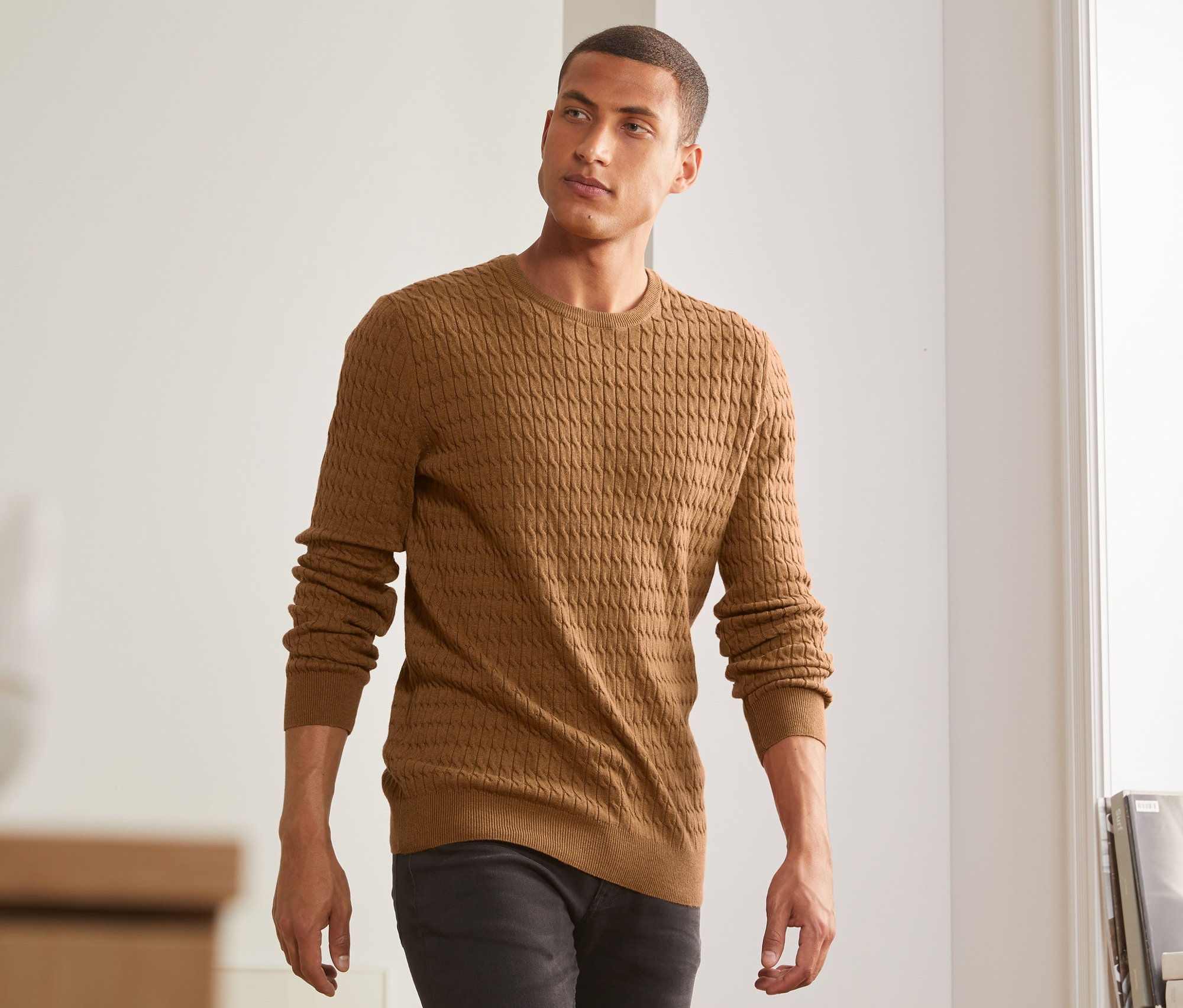Egy férfi melírozott, barna kötött pulóvert visel.