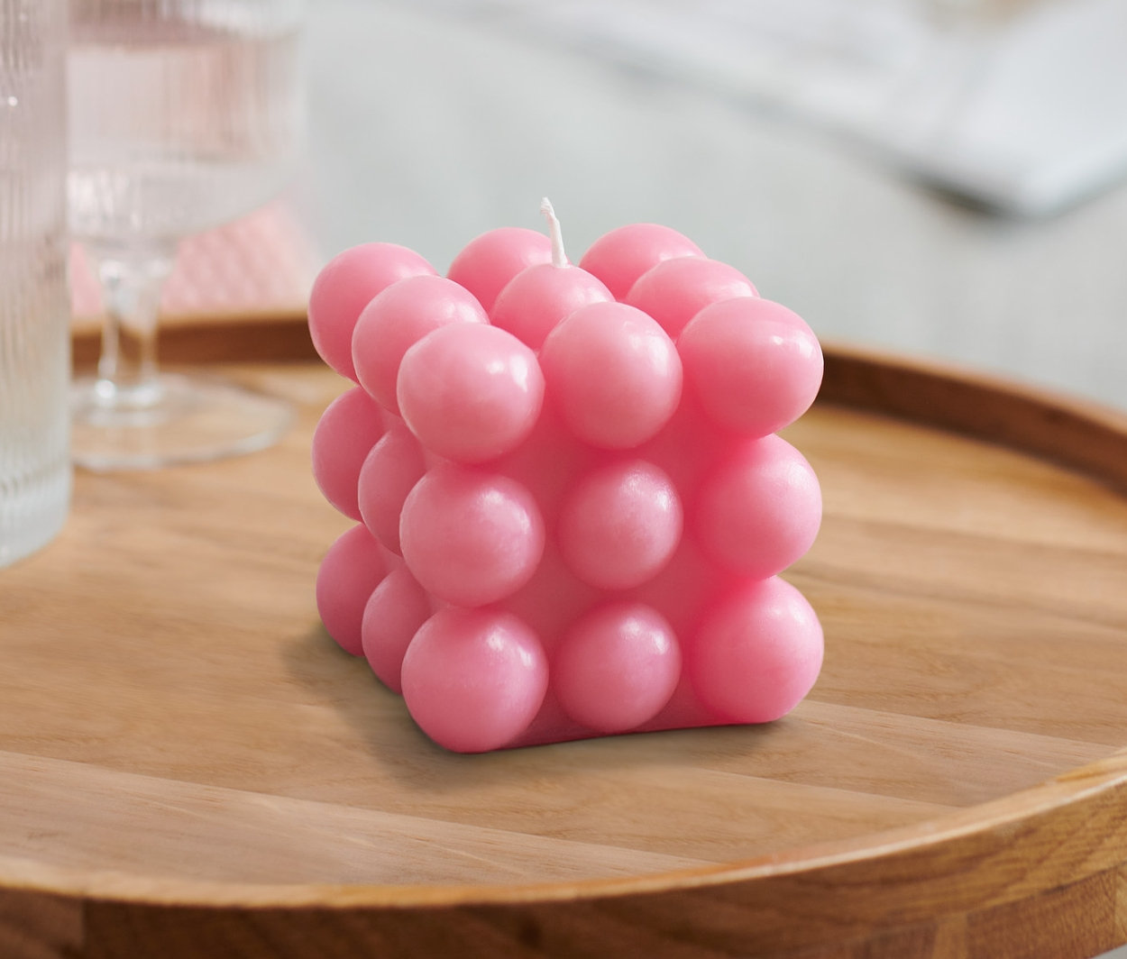 Egy fa asztalon 2 bubble gyertya, rózsaszín, egy pohár víz és egy üvegkancsó látható.