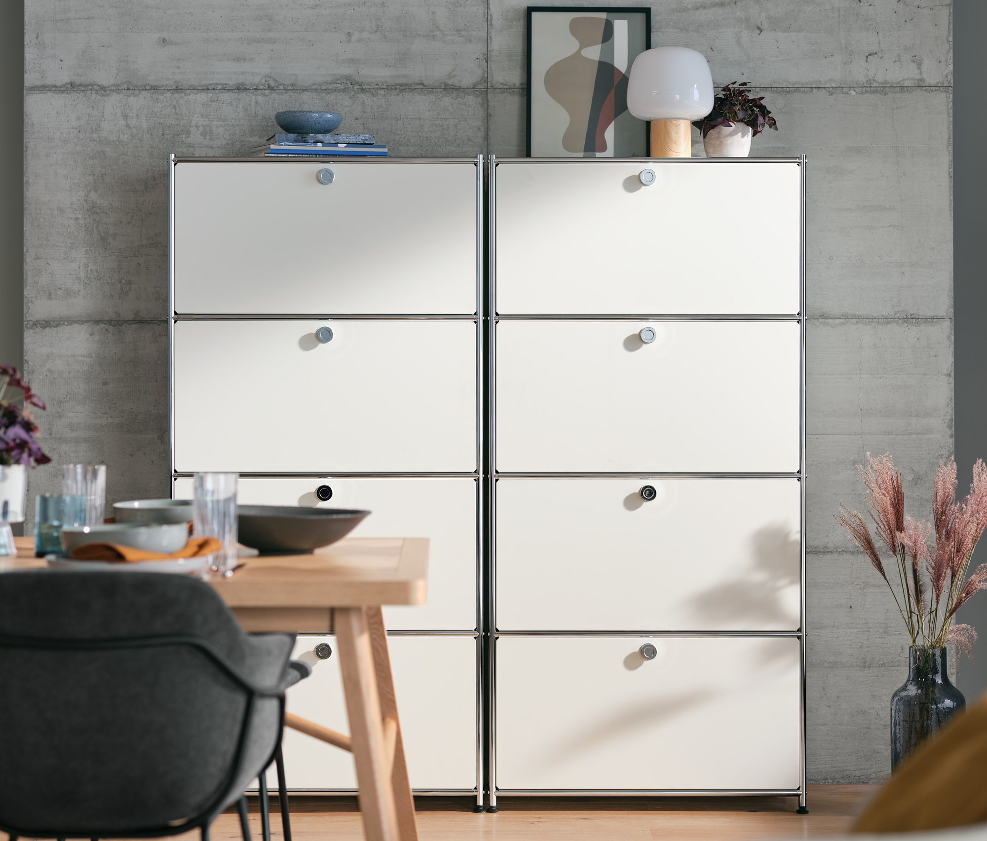 Két fehér magas fémpolc, 4 ajtóval egymás mellett áll egy étkezőasztal mögött.