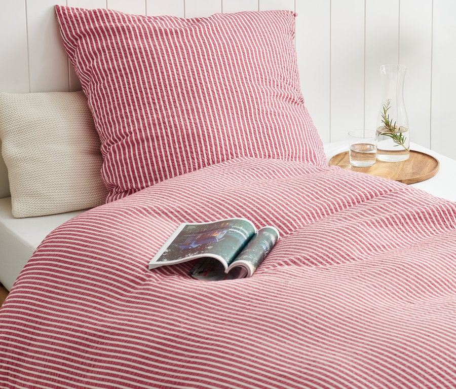 Egy piros-fehér csíkos krepp ágynemű van egy ágyon. Egy folyóirat van az ágyneműn.