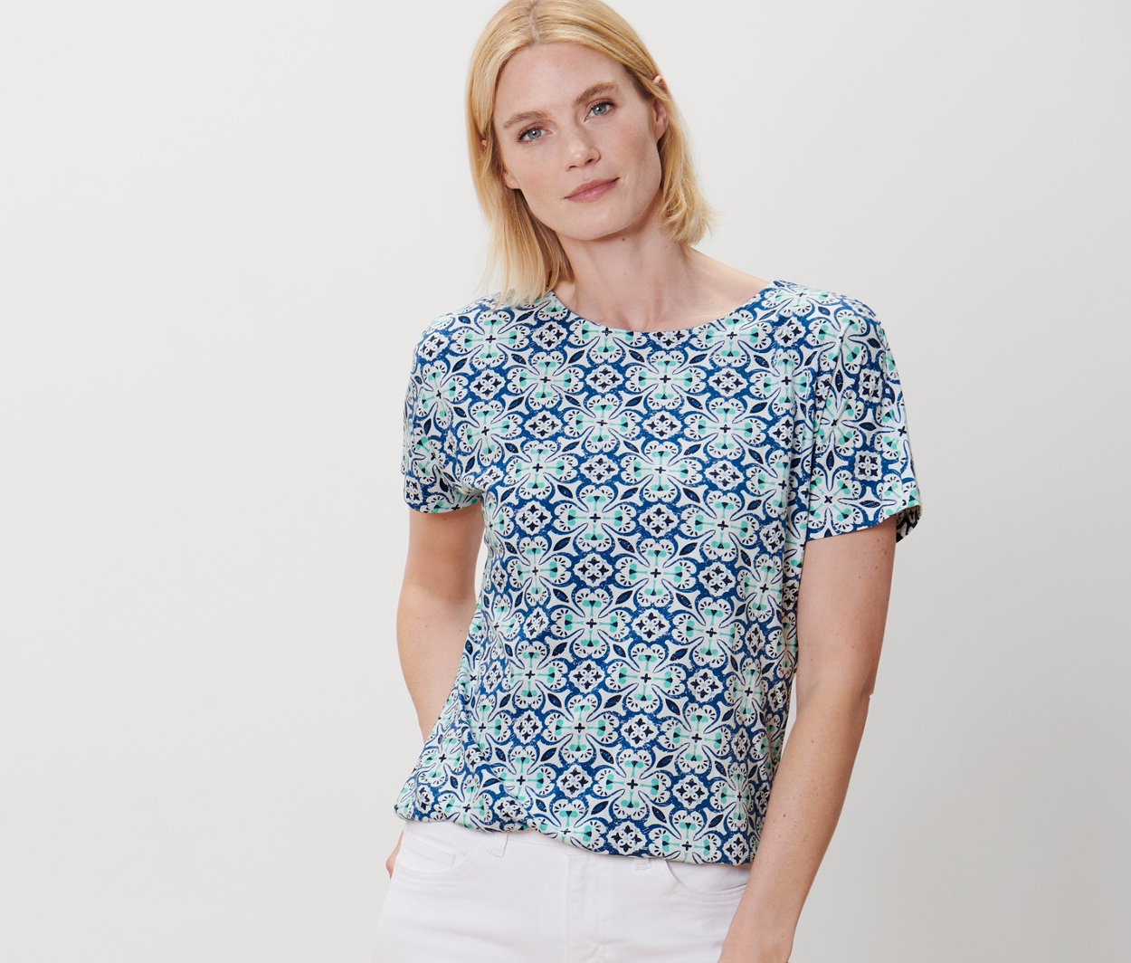 Nő pózol nyomott mintás pólóblúzban és fehér nadrágban.