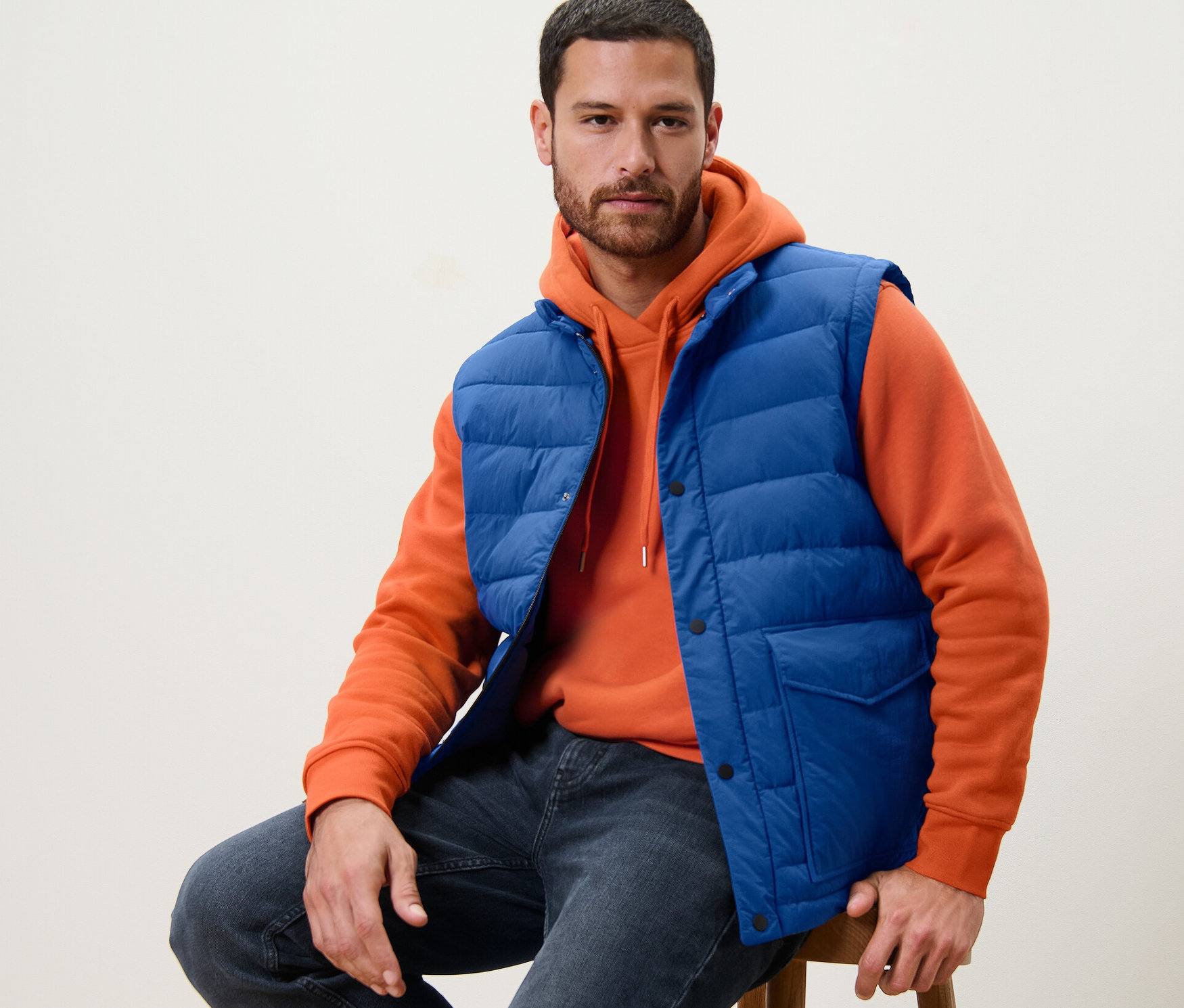 Férfi ül egy széken, kék steppelt mellényben.