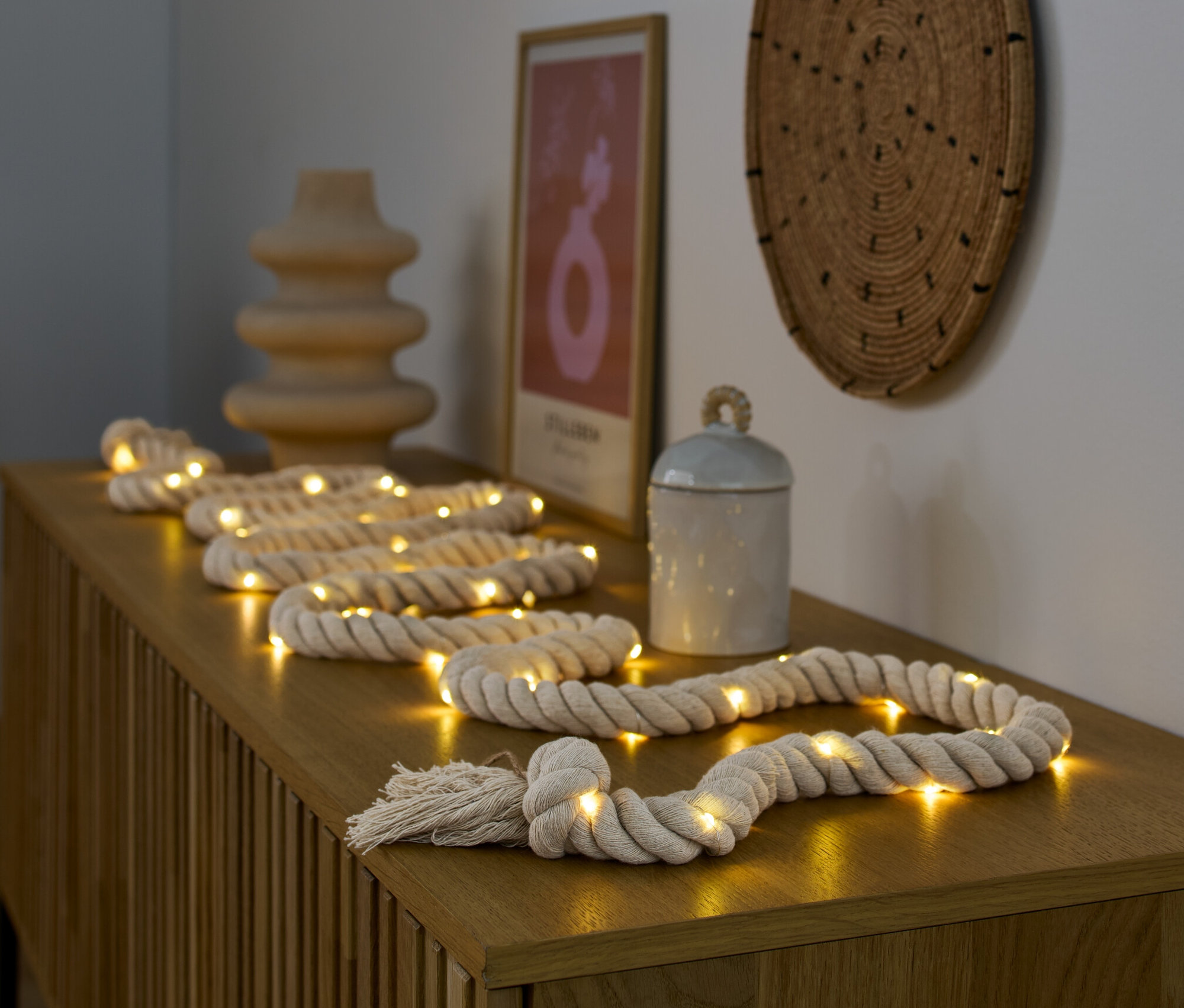 A LED-es kötél égősor egy fa komódon fekszik egy váza és egy doboz mellett.