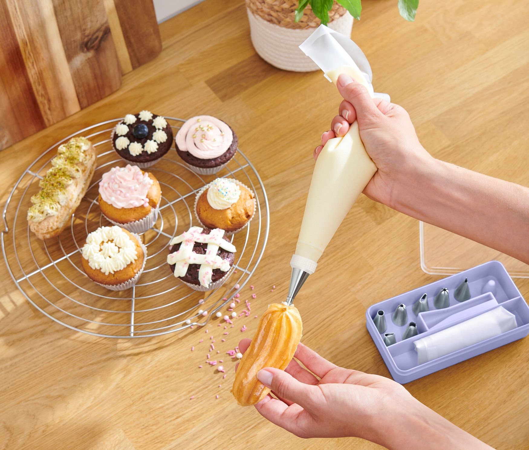 Egy személy édességet díszít krémekkel egy kinyomócső készlet segítségével. Az asztalon muffinok és egy tál gyümölcs található.