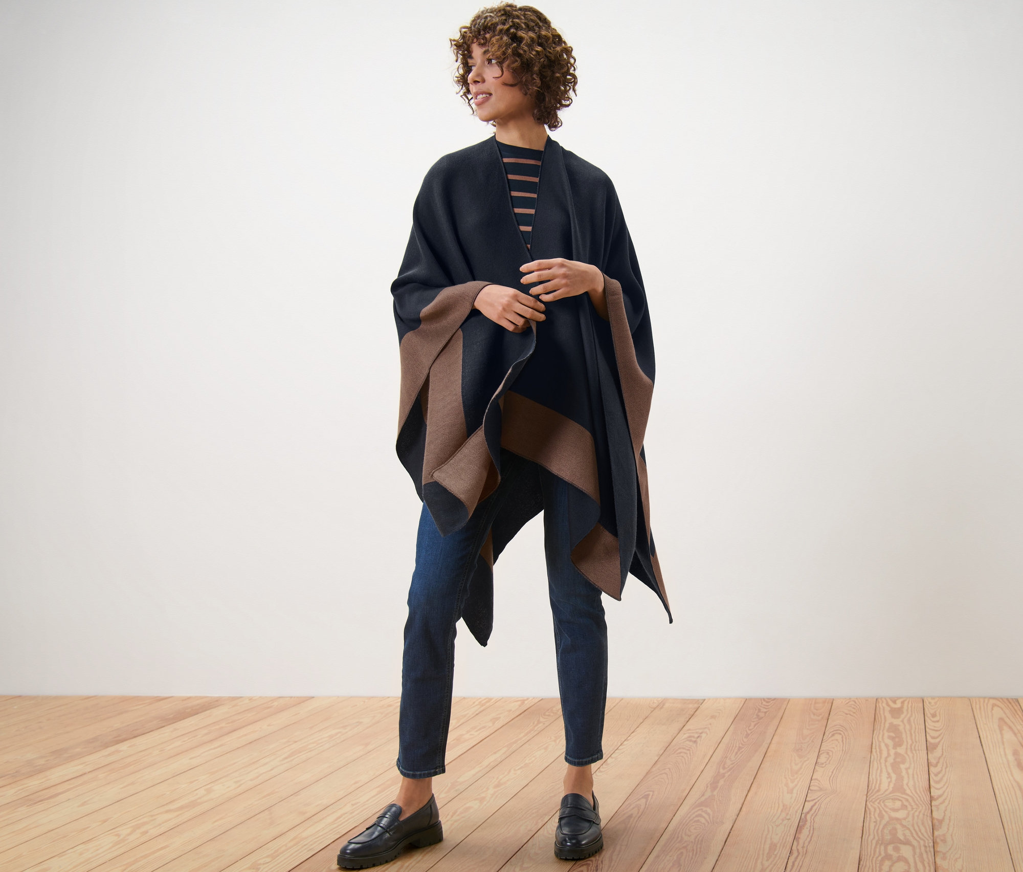 Nő áll a fapadlón, barna/fekete női kifordítható poncsót visel.