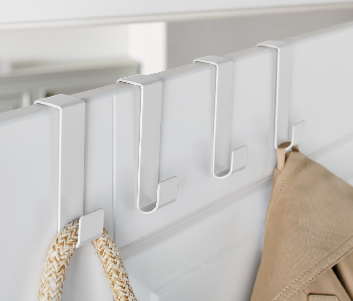 Három fehér akasztó van egy fehér ajtóra akasztva, rajtuk egy kabát és egy táska lóg.