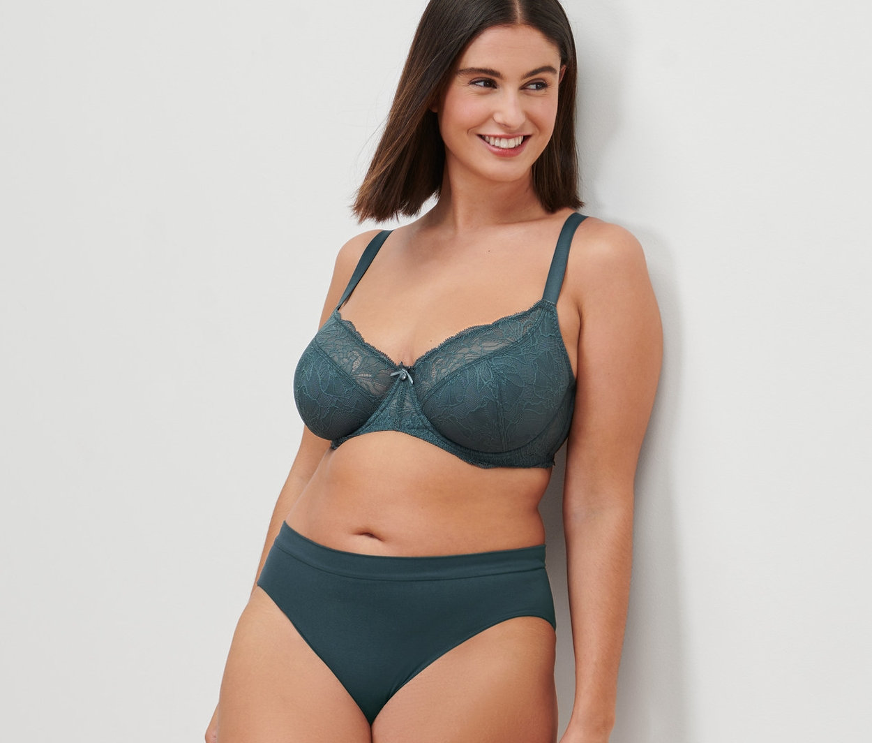 Egy falnak támaszkodó nő merevítős melltartót és alsóneműt visel.