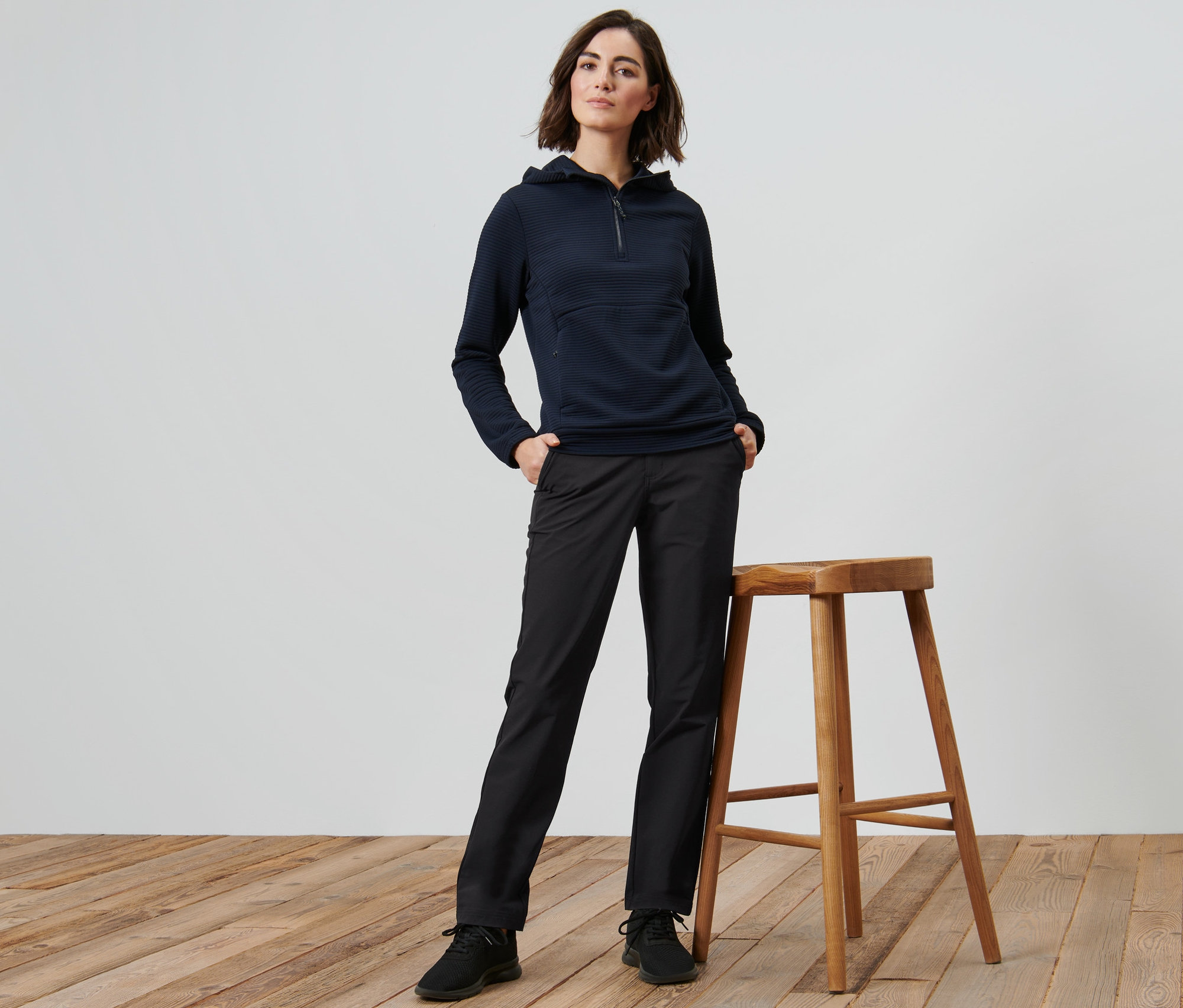 Nő pózol egy fa szék mellett, softshell nadrágot visel.