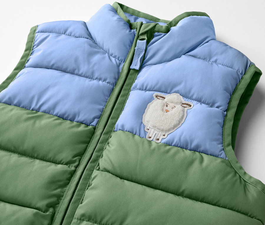 Egy zöld és kék színblokkos, bárány mintájú, kisgyerek steppelt mellény részlete.