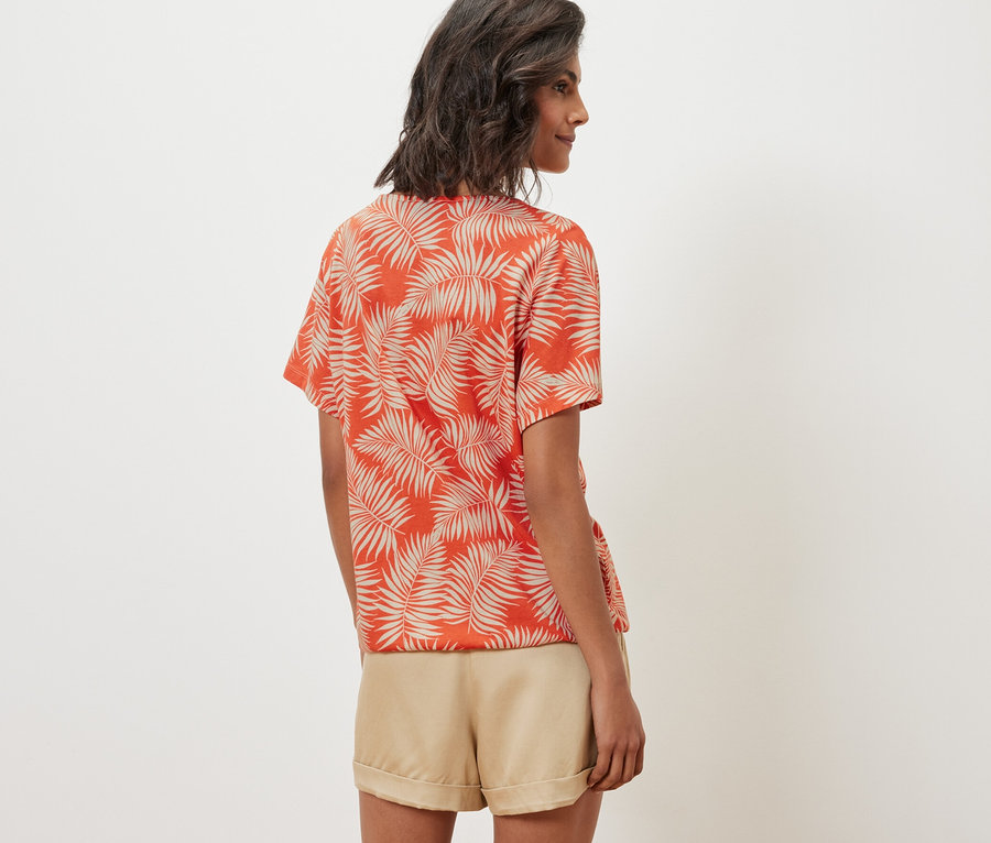 Nő visel egy nyomott mintás női pólóblúzt és rövidnadrágot.