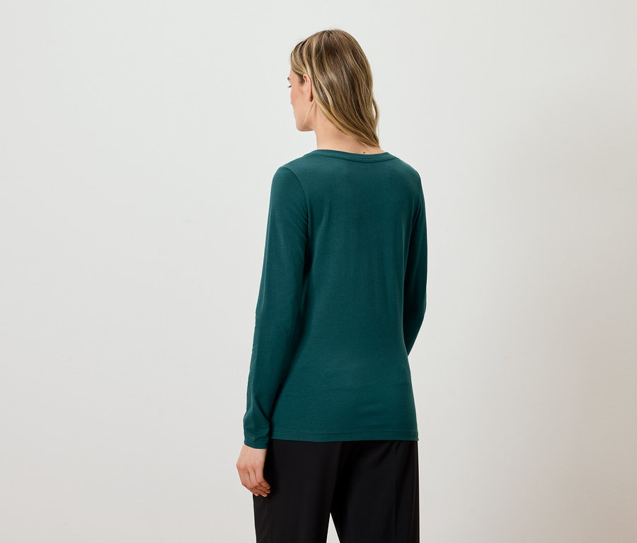 Hátulról látható egy szőke hajú nő, aki zöld, hosszú ujjú inget és fekete nadrágot visel.