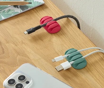 Az asztalon van két univerzális kábelrendező, egy rózsaszín és egy zöld, egy telefon és ceruzák mellett.