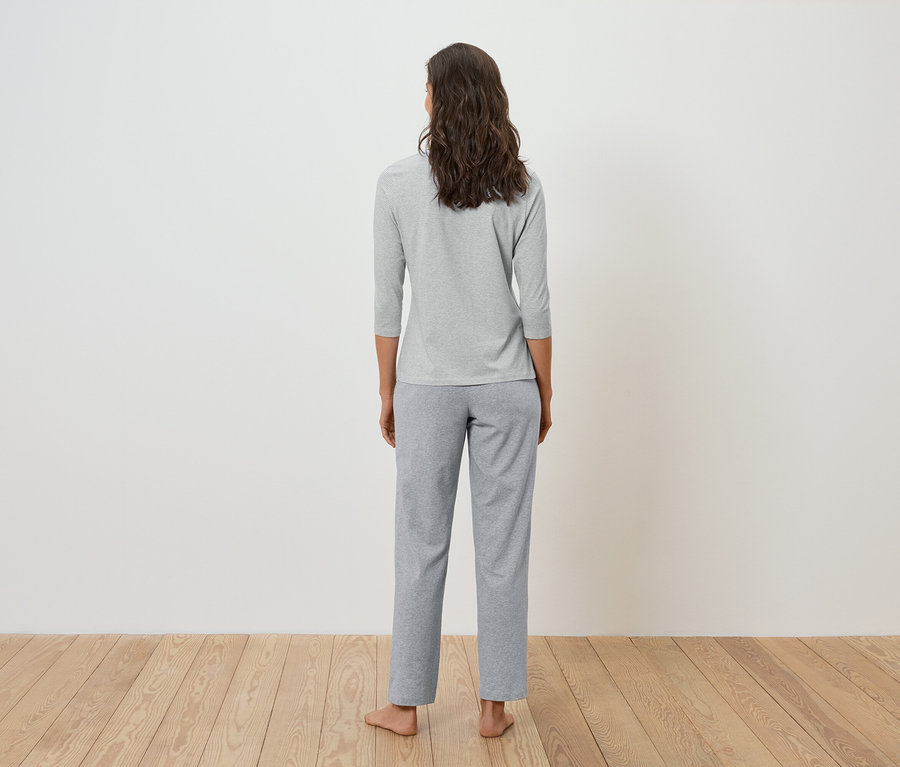 Hátulról látható egy barna, hullámos hajú nő szürke, háromnegyedes ujjú pólóban és szürke nadrágban.