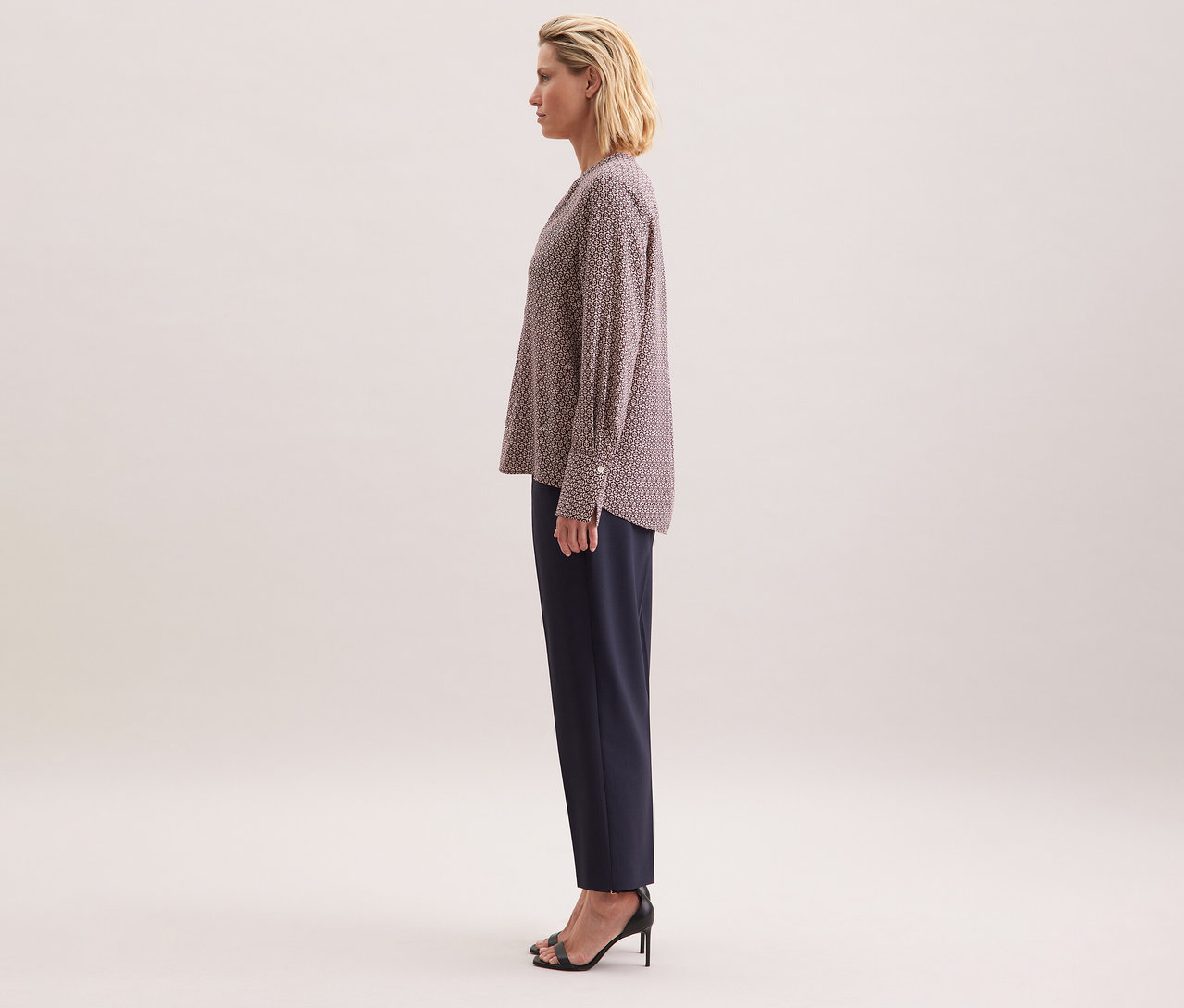 Nő visel ekrü-bordó mintás Seidensticker tunikát viszkózból, sötét nadrággal és fekete magas sarkú cipővel kombinálva.