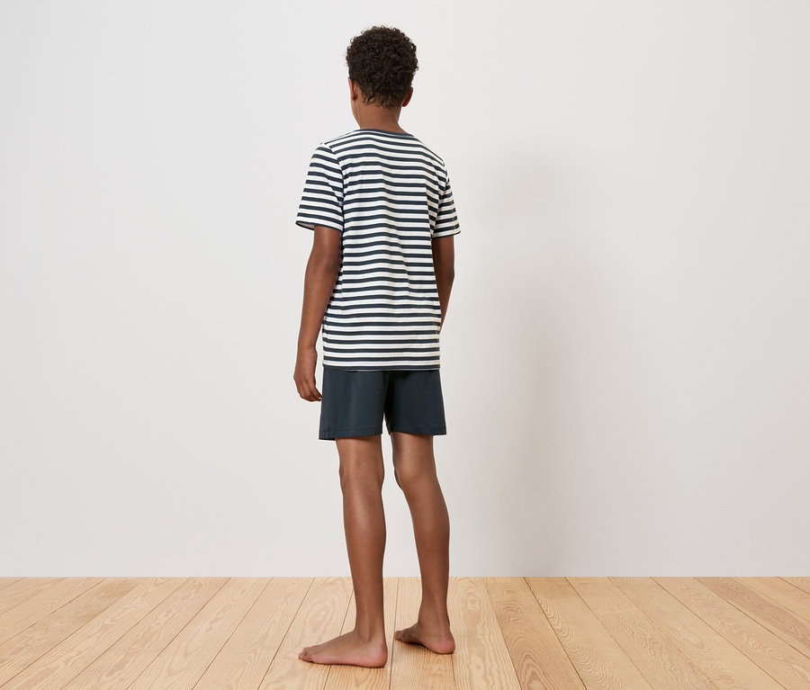 Fiú áll háttal, csíkos pólót és rövidnadrágot visel.