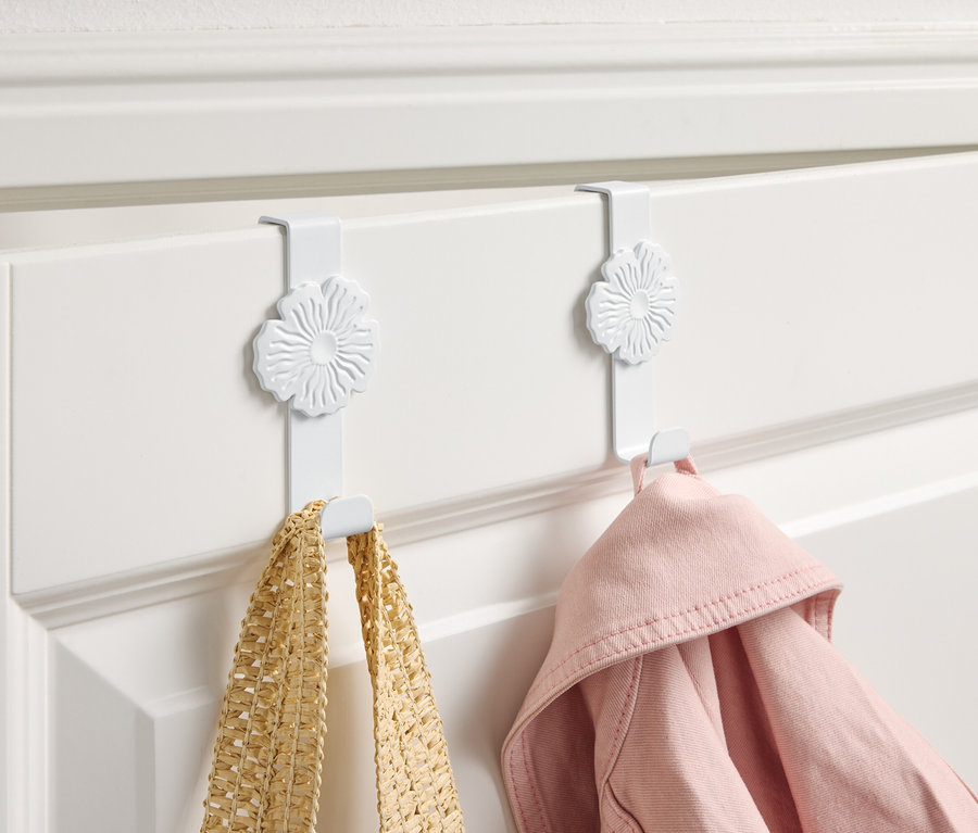 Két fehér, virágmintás akasztó lóg egy fehér ajtón, rajtuk egy sárga táska és egy rózsaszín kabát.