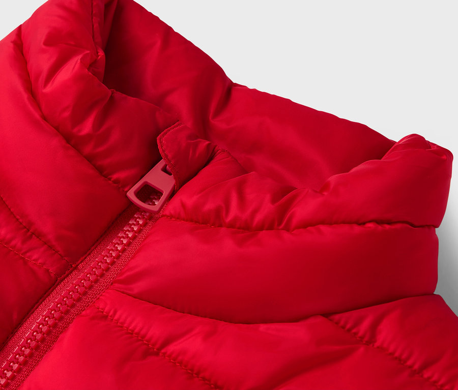 Egy piros, steppelt mellény részlete piros cipzárral.