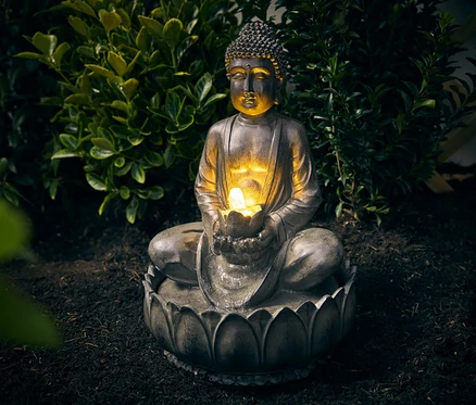 Buddha kerti csobogó ül a földön egy bokor előtt.