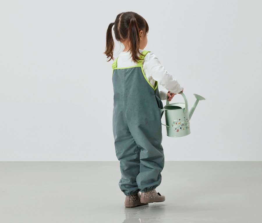 Kislány szürke nadrágban zöld kannát tart a kezében.