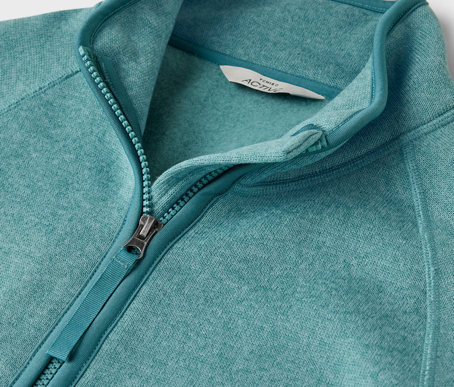 Közeli kép egy kékeszöld, cipzáras polár pulóverről.