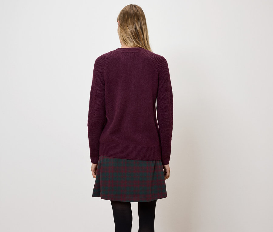 Hátulról látható nő bordó pulóvert és kockás szoknyát visel.