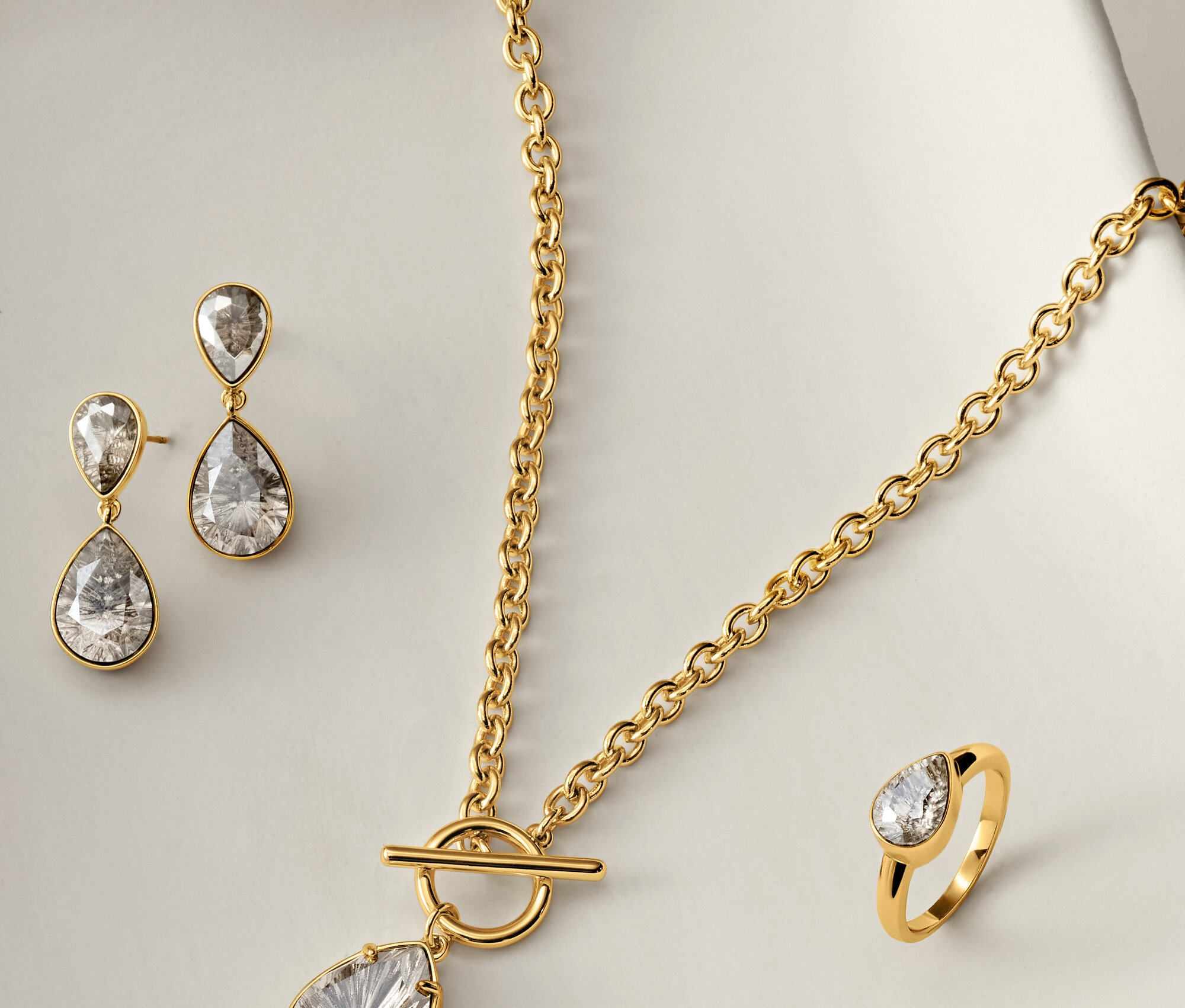Arany nyaklánc, fülbevaló és gyűrű áttetsző, csepp alakú kövekkel, fehér háttéren.