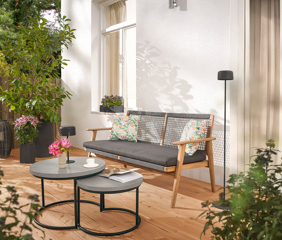 A teraszon egy kanapé párnákkal, két szürke asztal, egy állólámpa és növények találhatóak.
