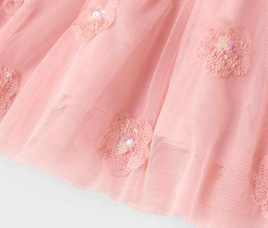 Egy rózsaszín tüllszoknya közeli képe flitteres virágokkal.