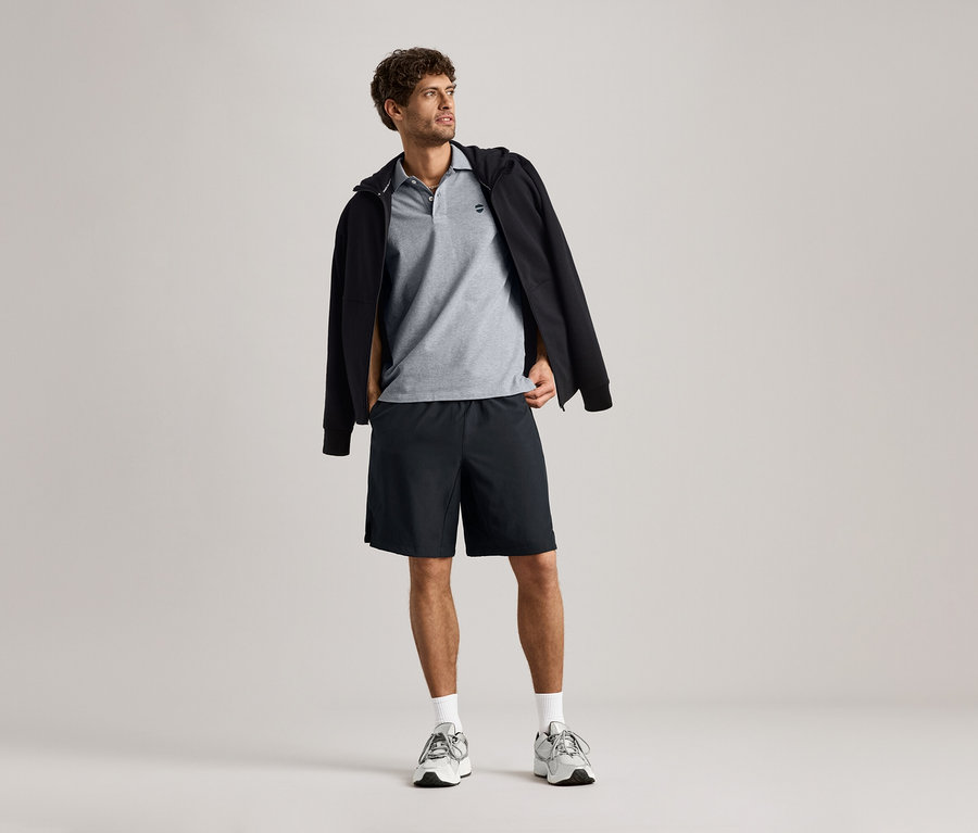 Férfi szabadidőfelsőt, szürke pólót és rövidnadrágot visel.