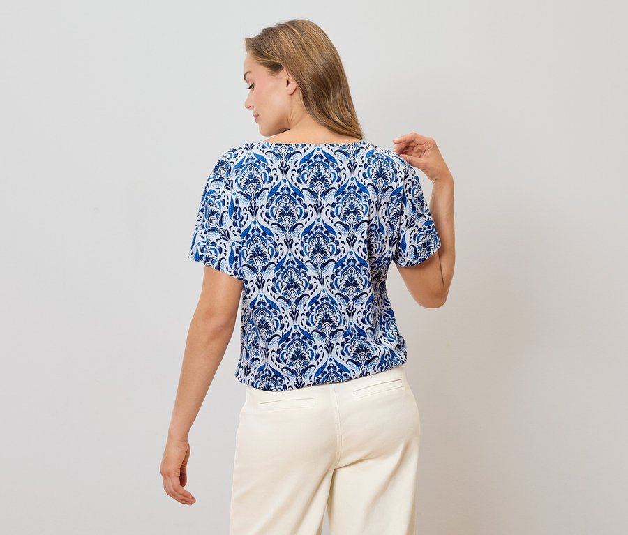 Hátulnézet egy szőke hajú nőről, aki kék-fehér mintás blúzt és világos nadrágot visel.